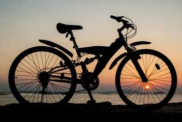 Fototapeta na wymiar Silhouette of mountain bike parking on jetty beside sea with sun