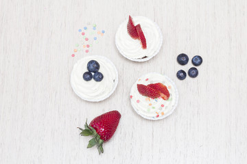 Three cupcakes with white cream, strawberries and blueberries