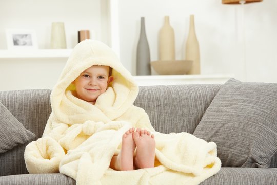 Smiling kid in bathrobe at home sofa bare feet