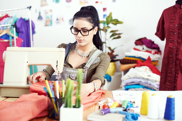 Young female fashion designer working on sewing machine