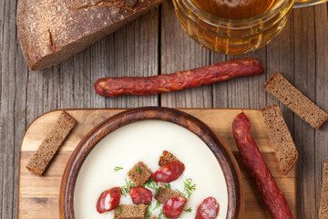 White cream beer soup with sausage in vintage wooden bowl with b