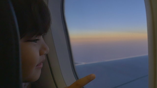 Happy little Asian girl looking outside the window of airplane