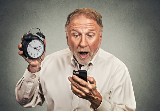 surprised business man with alarm clock looking at smart phone