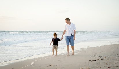 young happy father holding hand of little son walking on beach