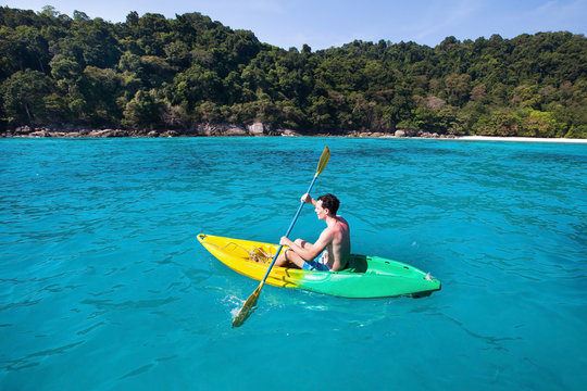 young caucasian man on kayak near paradise island in turquoise water