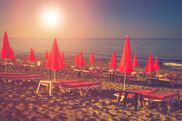 Red umbrellas and beach chairs on the beach in sunlight.