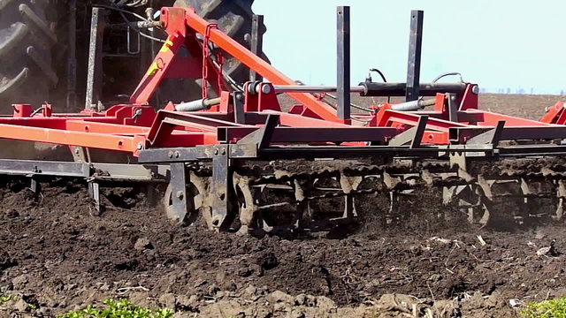 Tractor pulling land cultivating machine.