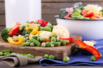 Frozen vegetables on cutting board, on napkin, on wooden table background
