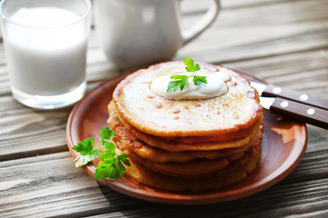 Stack of corn tortillas with stuffing, greens, cream and glass of milk on wooden table background