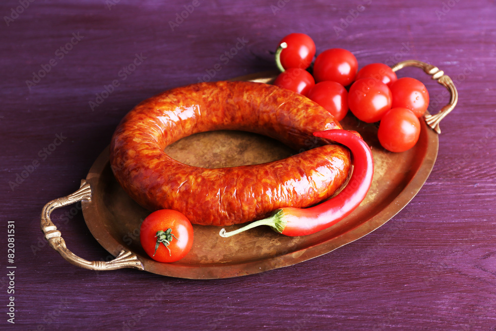 Poster Smoked sausage with cherry tomatoes and chili pepper on metal tray on color wooden table background