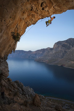 Male rock climber climbing along roof in cave, Kalymnos Island, Greece 