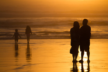 Parents watching kids silhouettes at sunset on beach