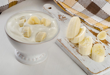 Yogurt with banana  in a white bowl   on white wooden table