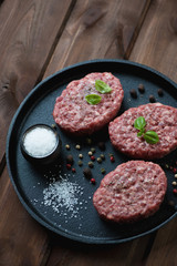 Frying pan with raw beef cutlets over wooden background
