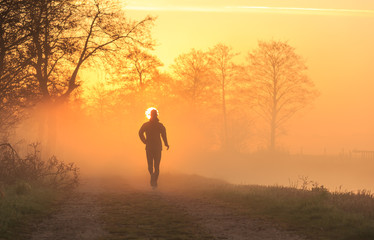 Runner on a gravel road during a foggy, spring sunrise.