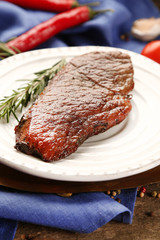 Composition with tasty roasted meat on plate, tomatoes and rosemary sprigs on wooden background