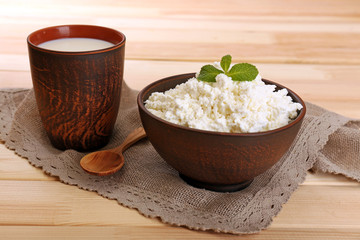Cottage cheese in bowl with cup of milk on wooden background