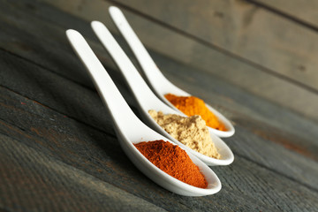 Different kinds of spices in spoons on wooden background