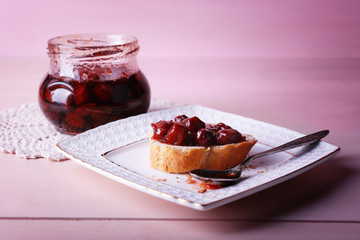 Fresh bread with jam on plate on wooden background
