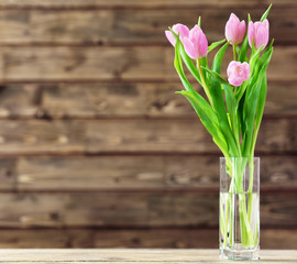 Beautiful pink tulips in vase on table on wooden background
