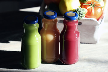 Bottles of juice with fruits and vegetables on table close up