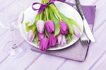 Purple tulip bouquet over plate on wooden table