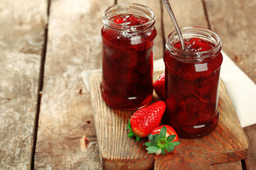 Jars of strawberry jam with berries on wooden background