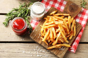 Tasty french fries on cutting board, on wooden table background