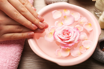 Female hands and bowl of spa water with flowers, closeup