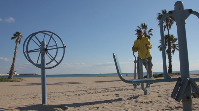 Young man on the beach exercising on cross trainer