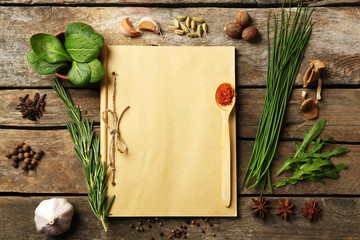 Open recipe book with fresh herbs and spices on wooden background