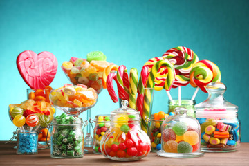 Colorful candies in jars on table on blue background