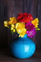 Colorful freesia in vase on wooden background