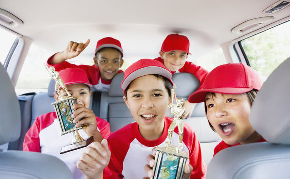 Multi-ethnic boys in car wearing baseball uniforms and holding trophies
