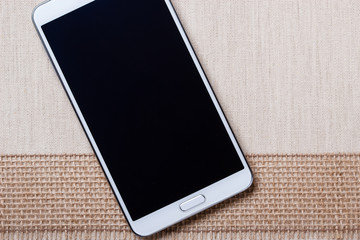 White modern smartphone with blank screen lies on textile.