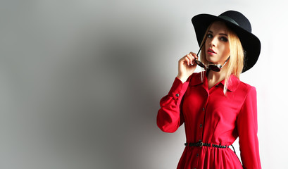 Expressive young model in red dress, black hat and sunglasses on gray background