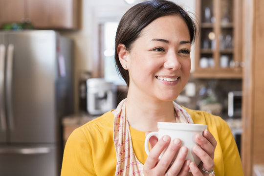 Mixed race woman having cup of coffee in kitchen