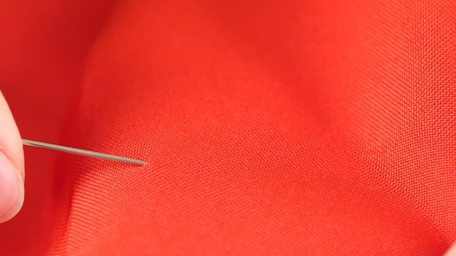 Woman sewing with needle and thimble on red cloth, close up
