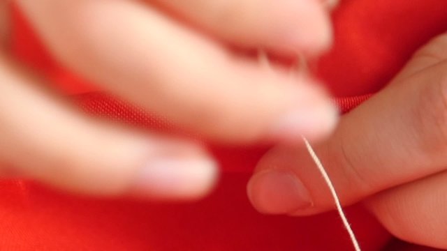 Woman`s hands sewing with needle, white thread and thimble on