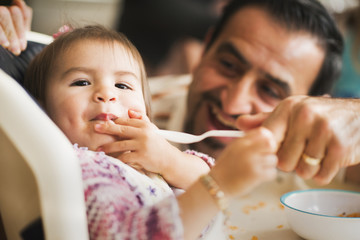 Hispanic father feeding daughter in high chair