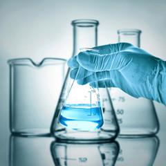 Flask in scientist hand with lab glassware background 