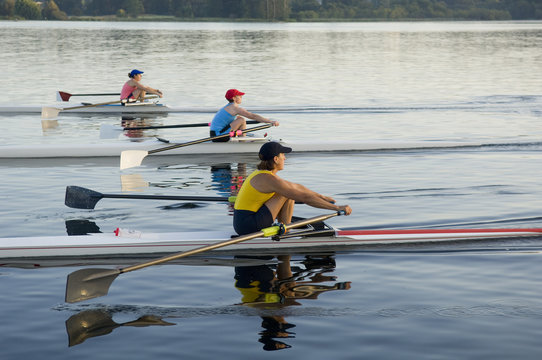 People rowing sculling boats on river