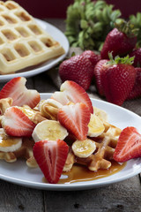 Waffles with bananas and strawberries covered with maple syrup
