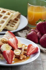 Waffles with bananas and strawberries covered with maple syrup
