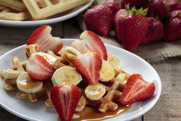 Waffles with bananas and strawberries covered with maple syrup