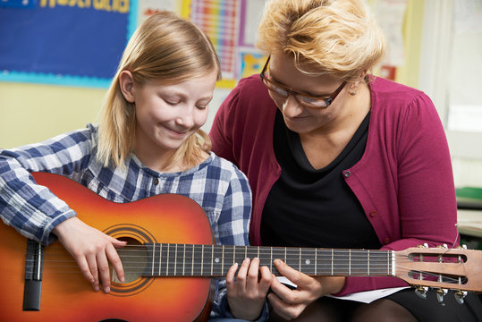 Teacher Helping Pupil To Play Guitar In Music Lesson