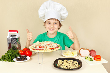 Young funny boy in chefs hat enjoys a cooking tasty pizza