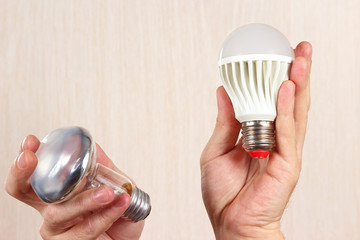 Hands compared incandescent bulb and ecofriendly led lamp