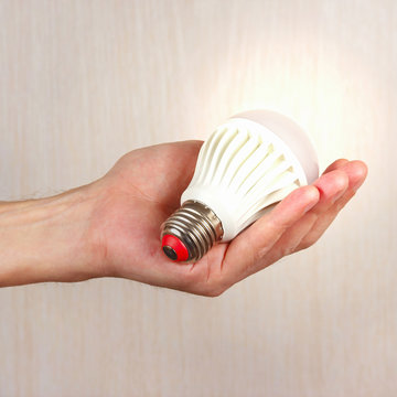 Hand holding a glowing bulb on a light wood background