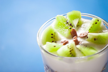 Kiwi and yogurt in glass, close up on blue background
